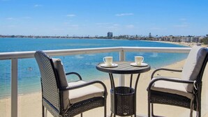 Uma varanda com cadeiras de vime e uma mesa pequena, com vista para a praia e o oceano.