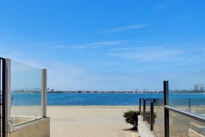 A beach view from a balcony with a clear sky, a sandy beach, and a calm sea. - New photos! Bayfront Penthouse plus parking+bikes! (San Diego)