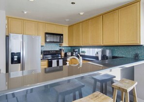 Une cuisine moderne avec des meubles en bois, un réfrigérateur en acier inoxydable, un four à micro-ondes et un îlot central en verre avec des tabourets.