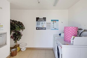 Ett tvättrum med tvättmaskin, torktumlare, en växt och en lista med regler för tvättrummet som är uppsatt på väggen.