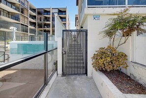 A gated entrance to a residential building with a clear glass barrier, a small bush, and a sign indicating video surveillance.