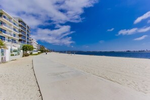 A beach with a white sandy shore, a clear blue sky, and a row of multi-story buildings with balconies.