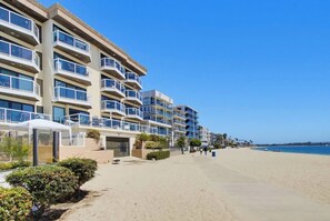 Un hôtel situé en bord de mer, doté de nombreux balcons, d’une plage de sable et offrant une vue sur un ciel bleu azur.