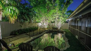 A backyard with a swimming pool, surrounded by a wooden fence and trees. There are Adirondack chairs and a table near the pool. - Oasis in the heart of Equestrian country (Wellington)