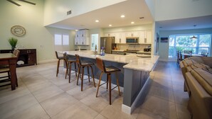 A modern kitchen with a large island, bar stools, and a dining area with a sofa. - Oasis in the heart of Equestrian country (Wellington)