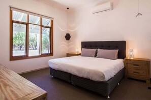 Un dormitorio con un ventanal grande, una cama, mesitas de noche y una lámpara colgante.