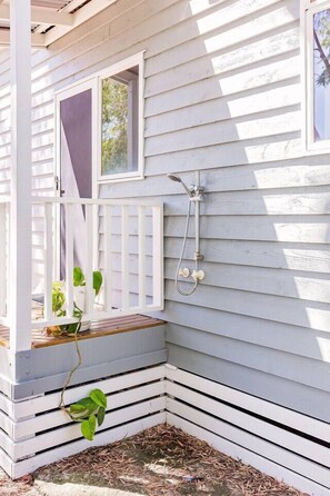 A white wooden house with a porch, a window, and a showerhead mounted on the wall.