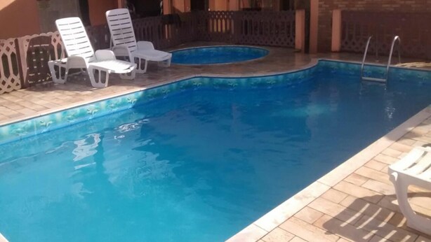 A rectangular swimming pool with clear blue water, surrounded by a tiled deck. There are white lounge chairs along the poolside. - House with pool 200 meters from the beach (Prainha)