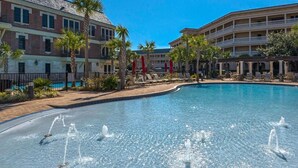 Una piscina con fuentes, rodeada de palmeras y un edificio con varios balcones.