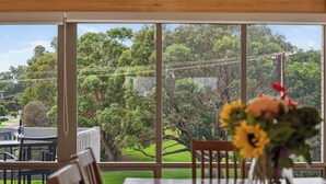 A dining area with a table, chairs, and a view of a lush garden through large windows. - 4/1 Harbour View Terrace - Wi-Fi (Victor Harbor)