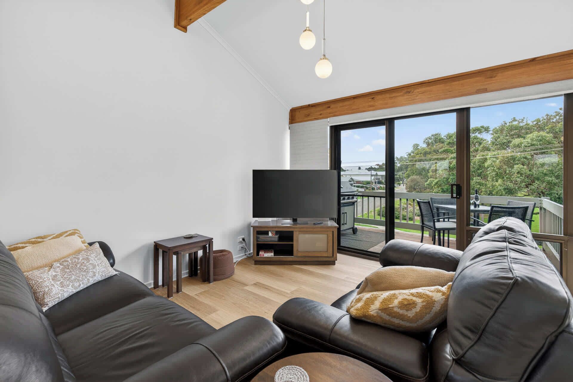A modern living room with a leather sofa, a flat-screen TV, and a balcony with outdoor furniture.