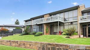 A two-story residential building with a balcony, large windows, and a stone retaining wall. - 4/1 Harbour View Terrace - Wi-Fi (Victor Harbor)