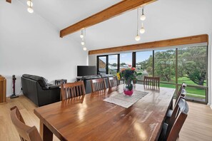 A spacious dining area with a large wooden table, multiple chairs, a television, and a view of the outdoors.