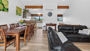 A spacious living area with a dining table, leather sofa, and a kitchen in the background. - 4/1 Harbour View Terrace - Wi-Fi (Victor Harbor)