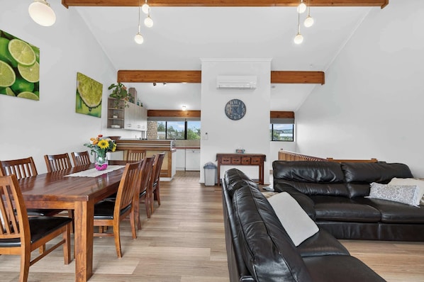 A spacious living area with a dining table, leather sofa, and a kitchen in the background.