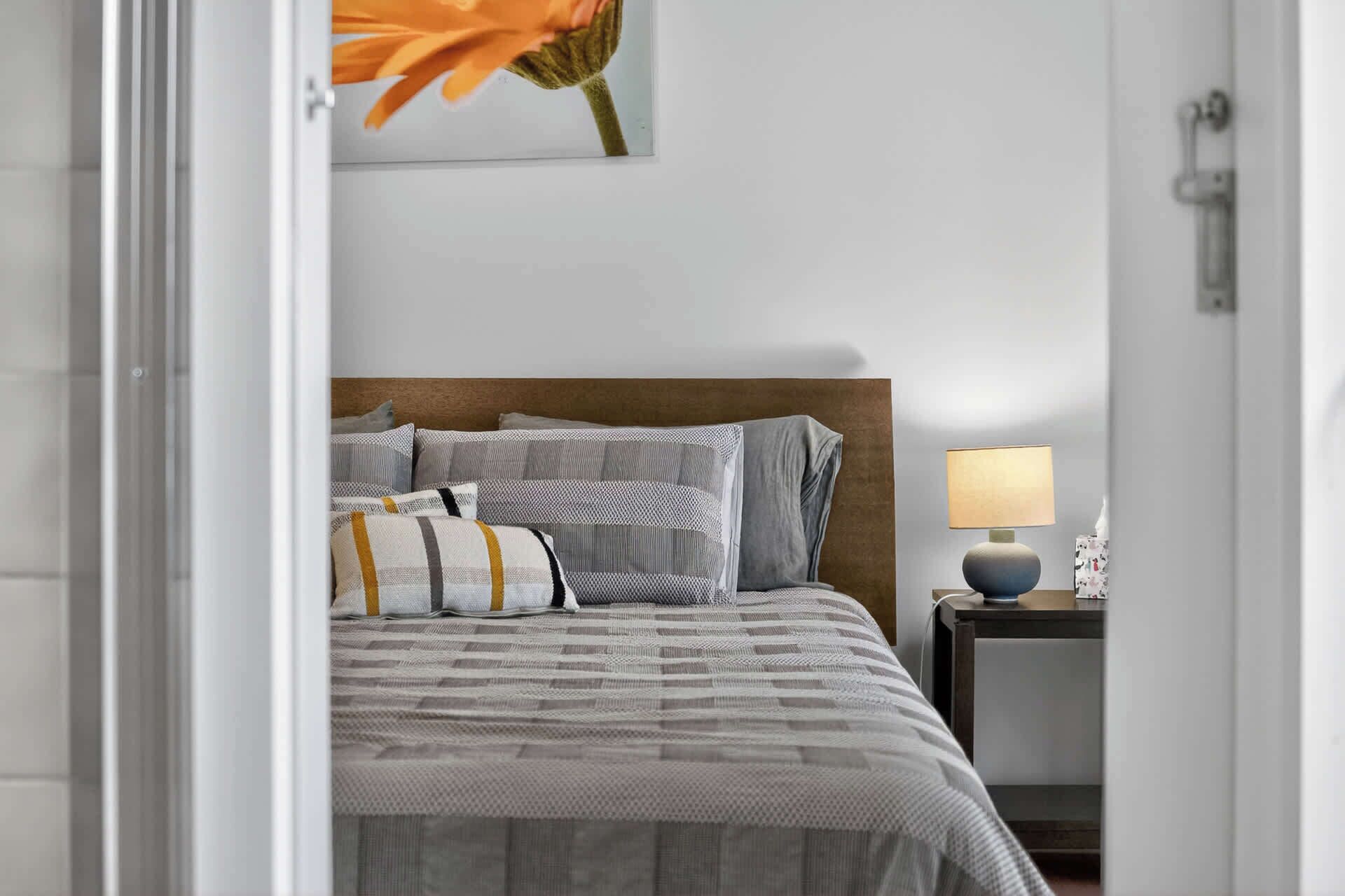 A neatly arranged bedroom with a bed, pillows, a bedside table with a lamp, and a wall-mounted artwork.