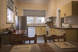 A compact kitchen with a dining area, featuring a refrigerator, microwave, oven, and a window with blinds. - The Gatehouse@ Beechworth (Beechworth)