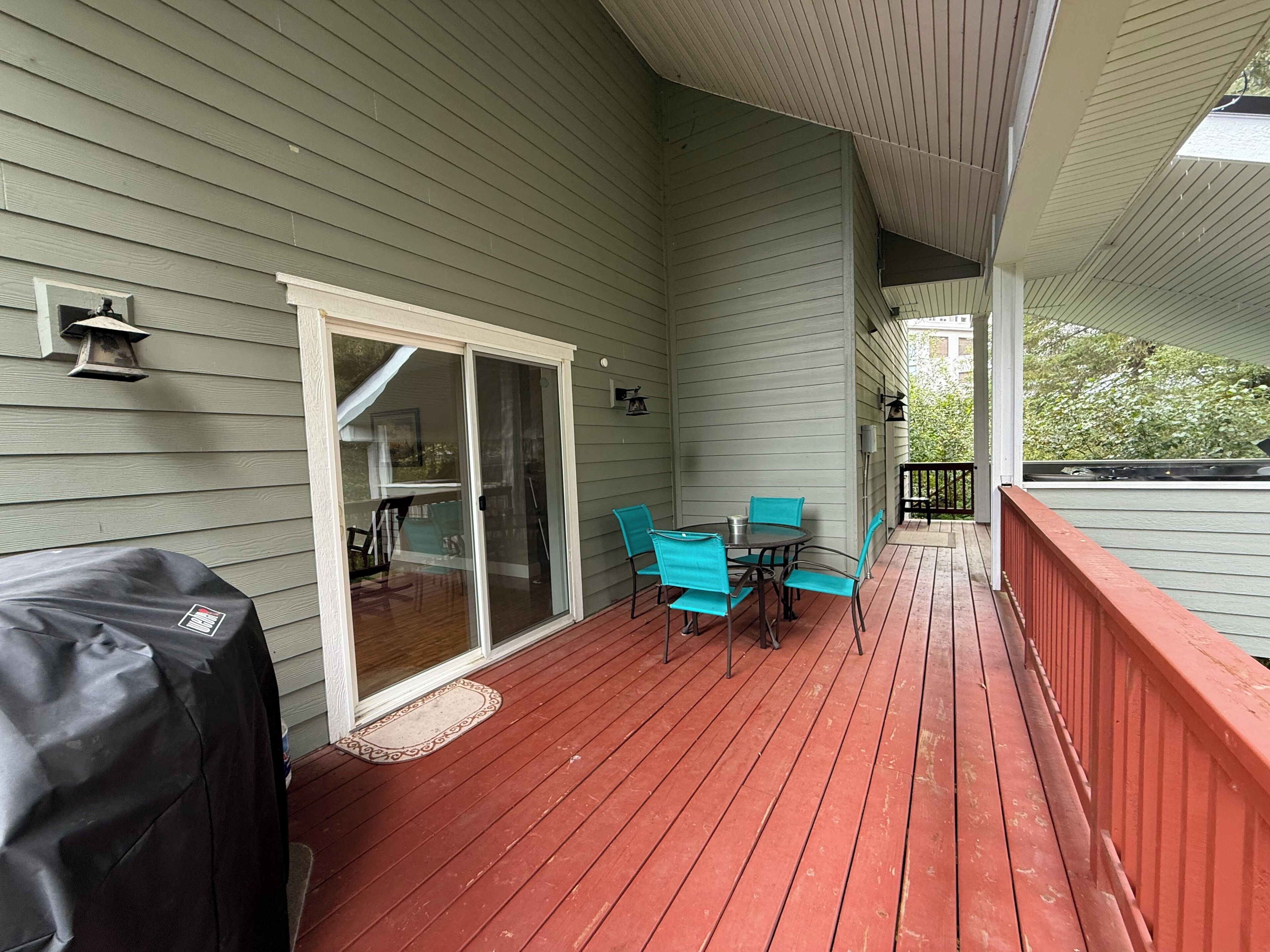 A covered deck with a red railing, a grill, and a table with chairs.