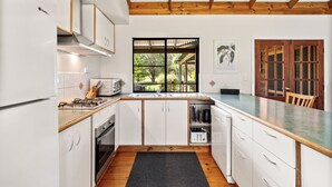 A modern kitchen with white cabinetry, a wooden ceiling, and a window overlooking a garden.