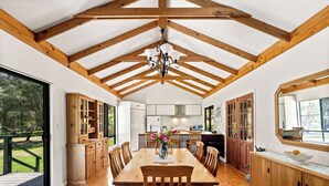 A spacious kitchen with wooden beams, a dining area with a large table and chairs, and a view of a garden through the windows.