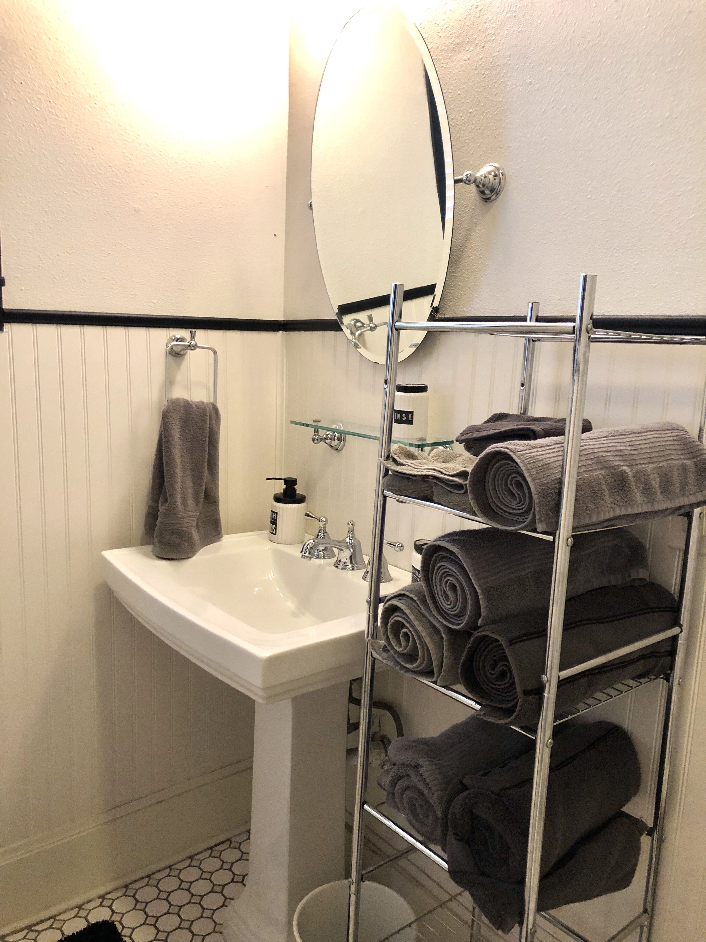 Un baño con lavamanos blanco, un espejo y un perchero con varias toallas.
