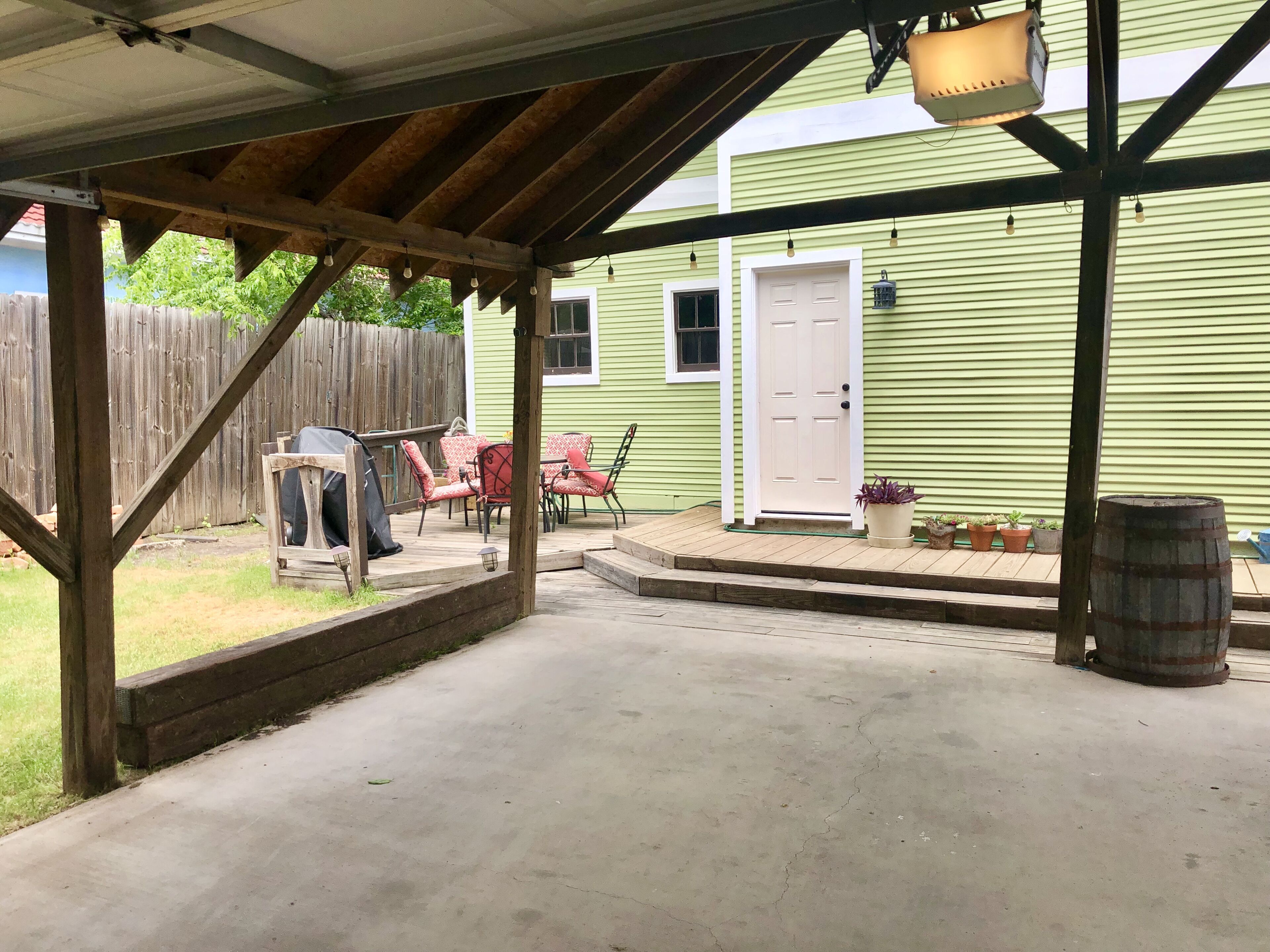 Eine überdachte Terrasse mit Holzboden, Gartenmöbeln und einem Grill.