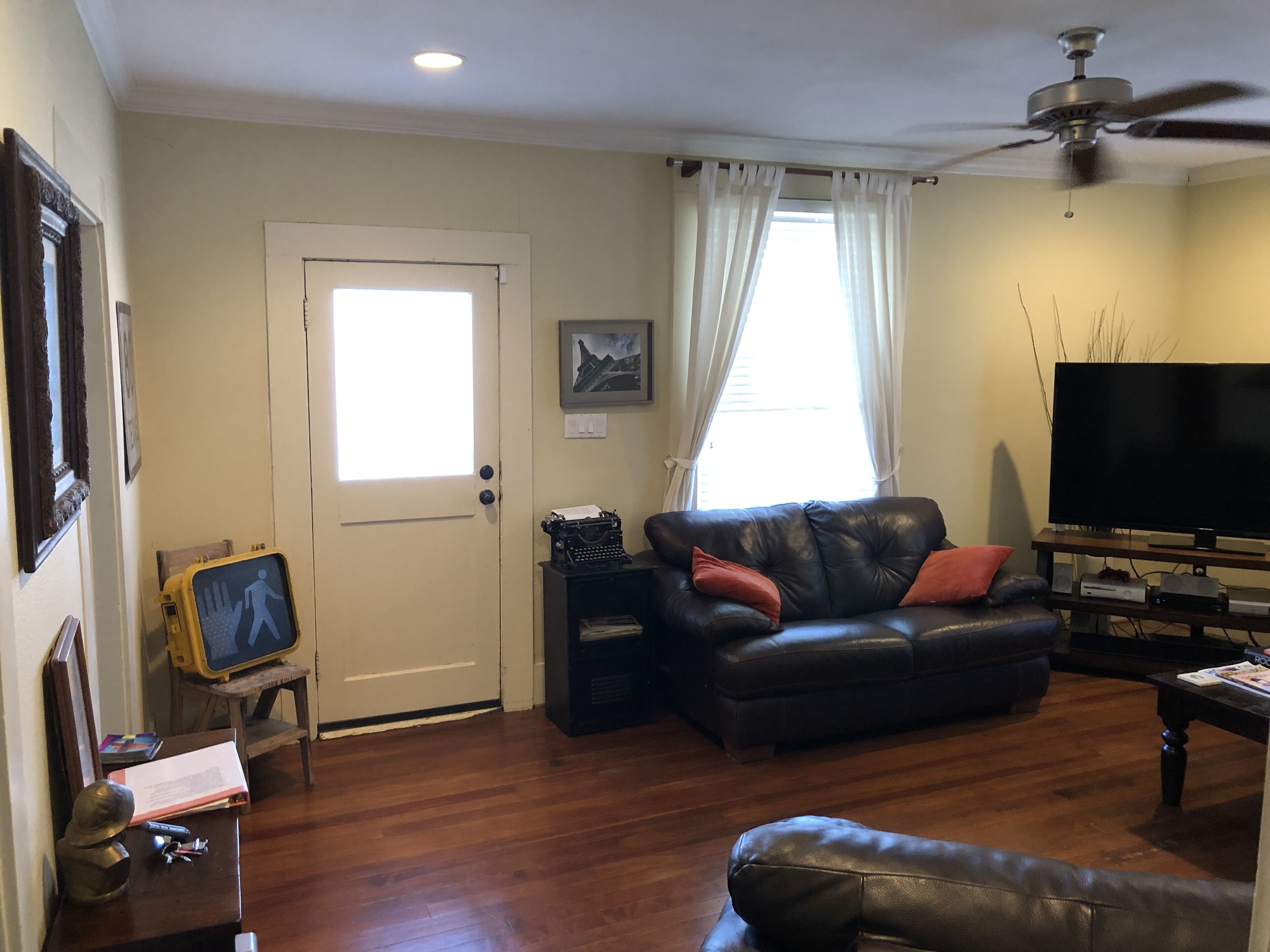 A living room with a black leather sofa, a television, a ceiling fan, and a door with a window.