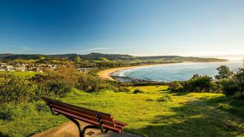 Un banco con vista a un paisaje costero, incluyendo la playa y colinas.