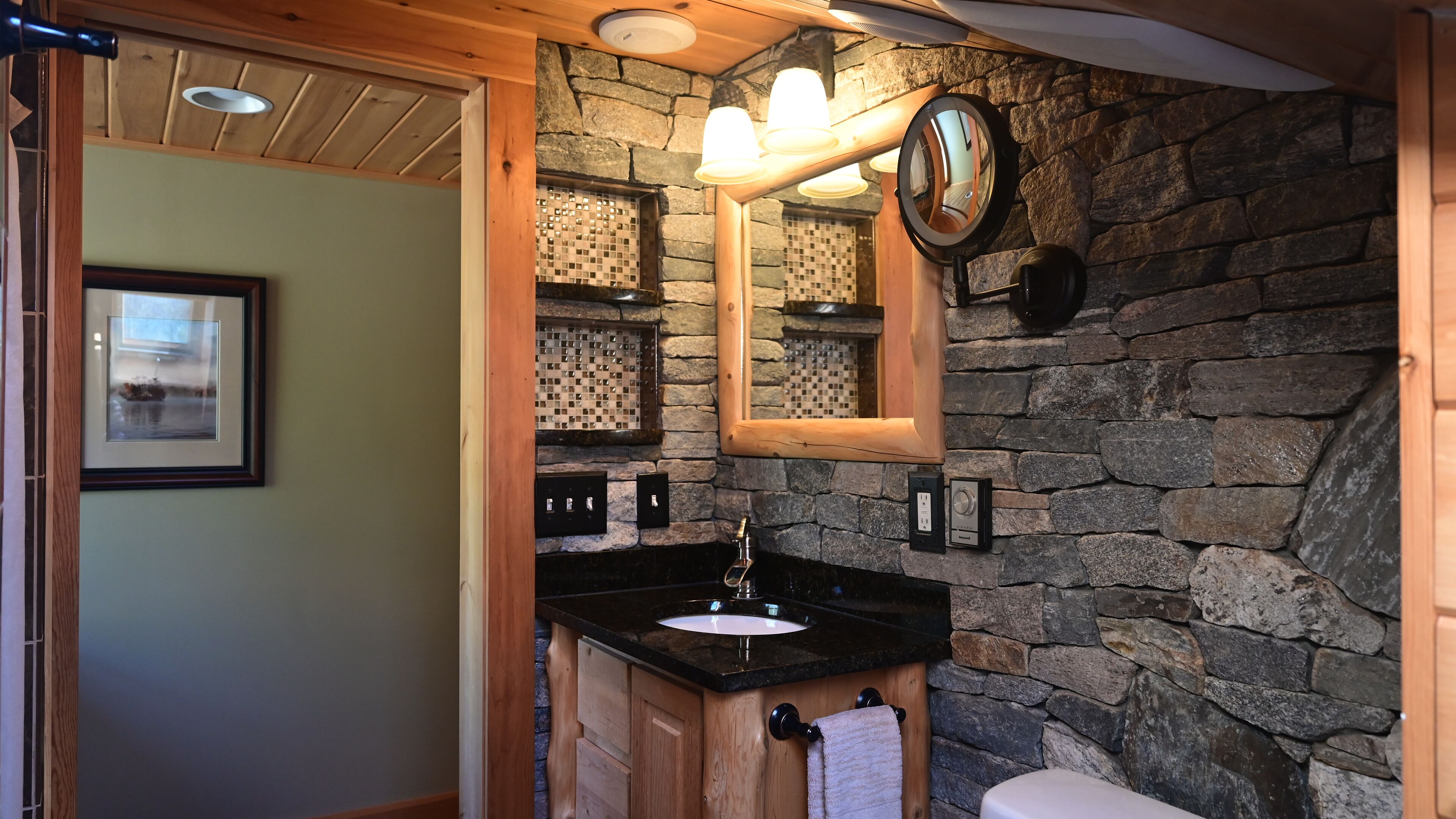 Une salle de bain avec un mur en pierre, des meubles en bois, un lavabo et un miroir.