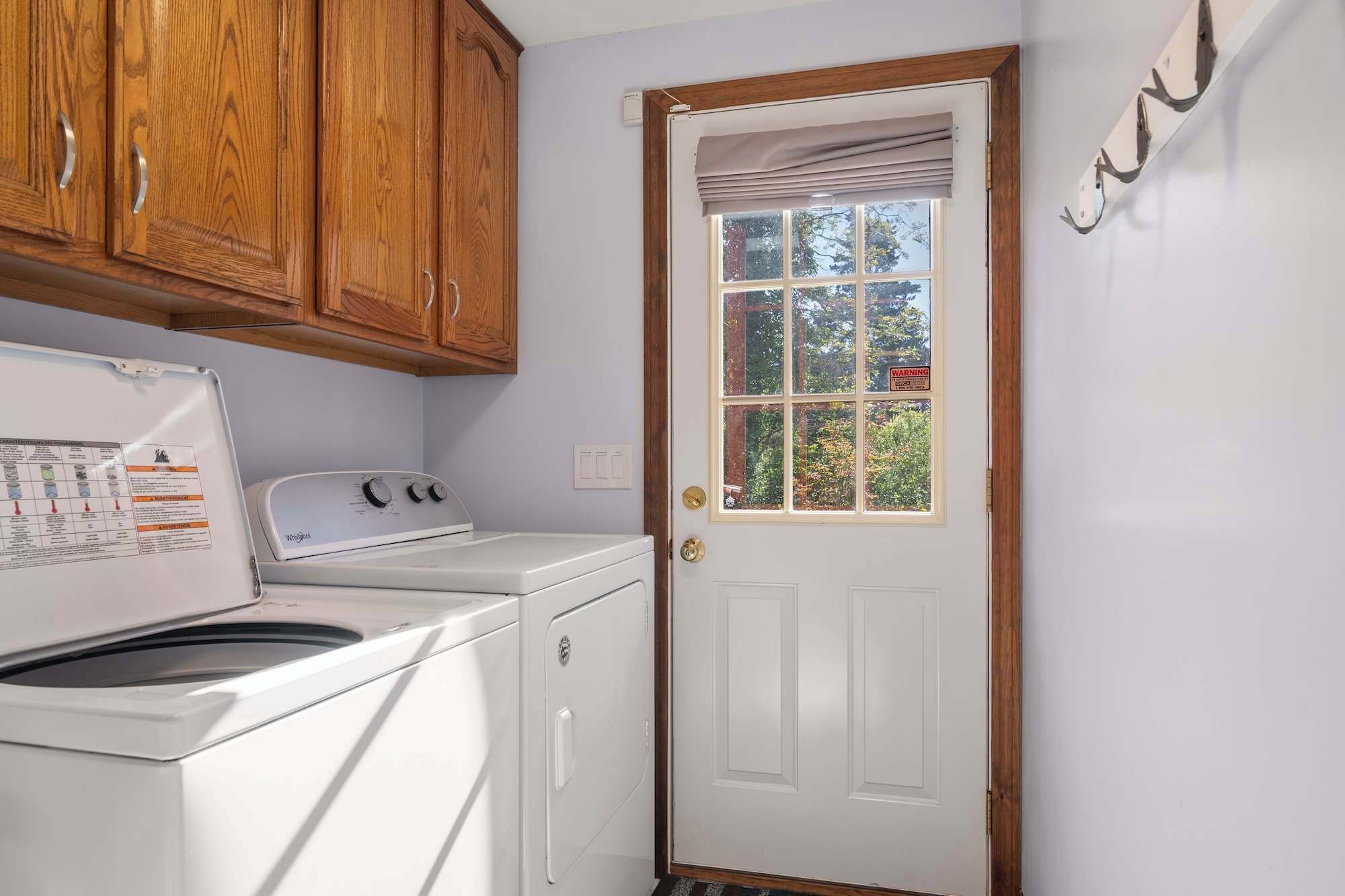 A laundry room with a washer and dryer, wooden cabinets, a white door with a window, and a 'No Smoking' sign.