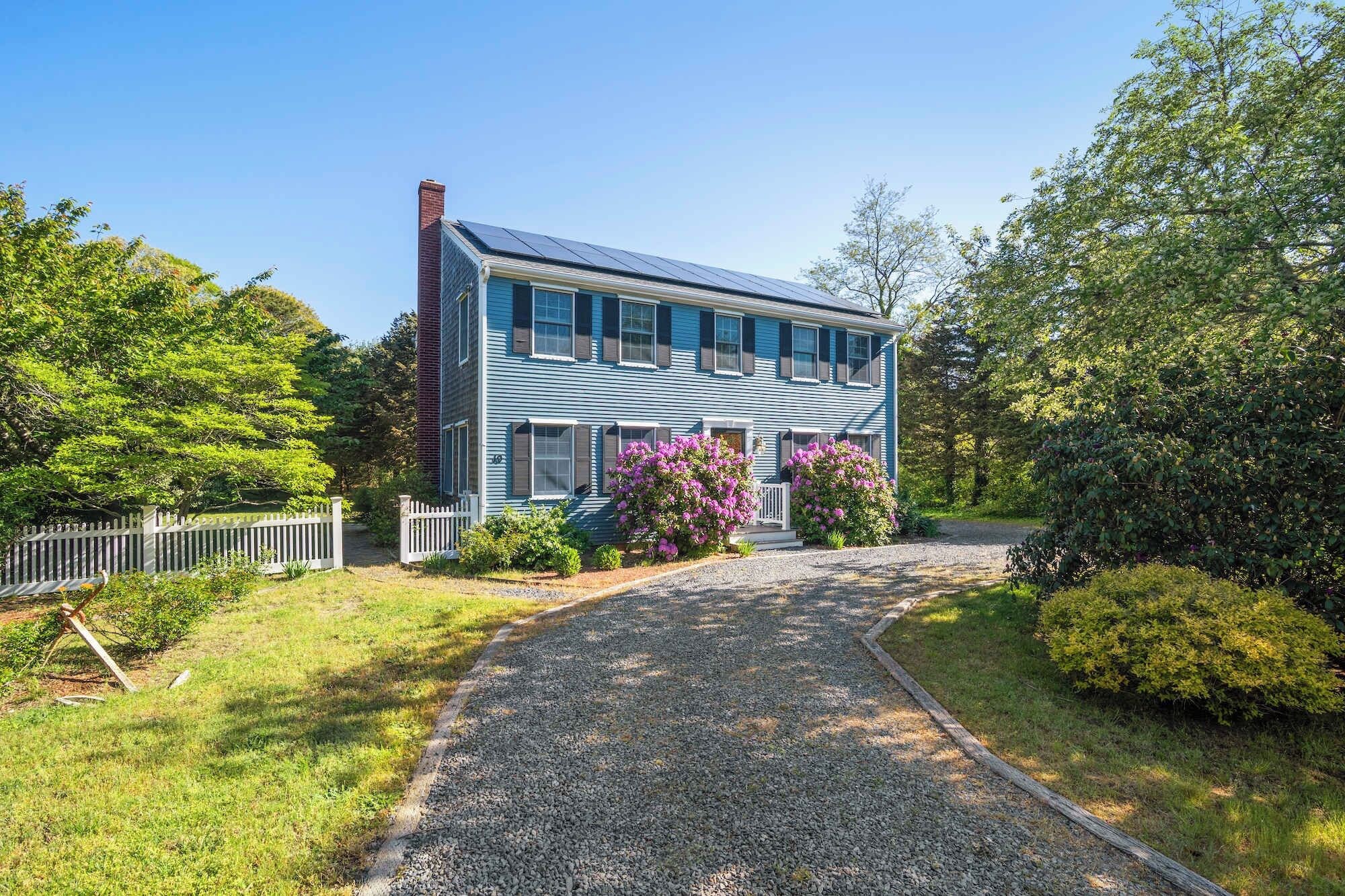 A two-story house with a gravel driveway and a white picket fence.