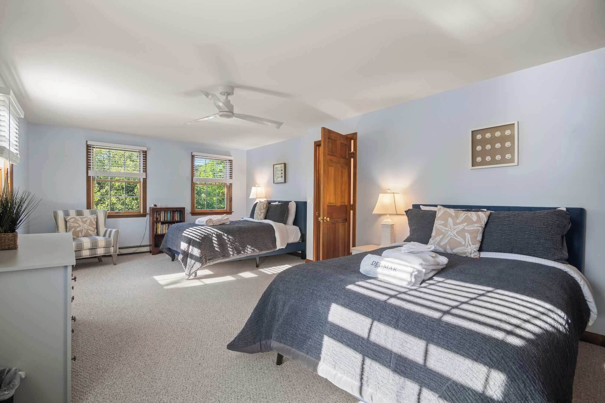 A bedroom with two beds, a ceiling fan, and a large window with blinds.