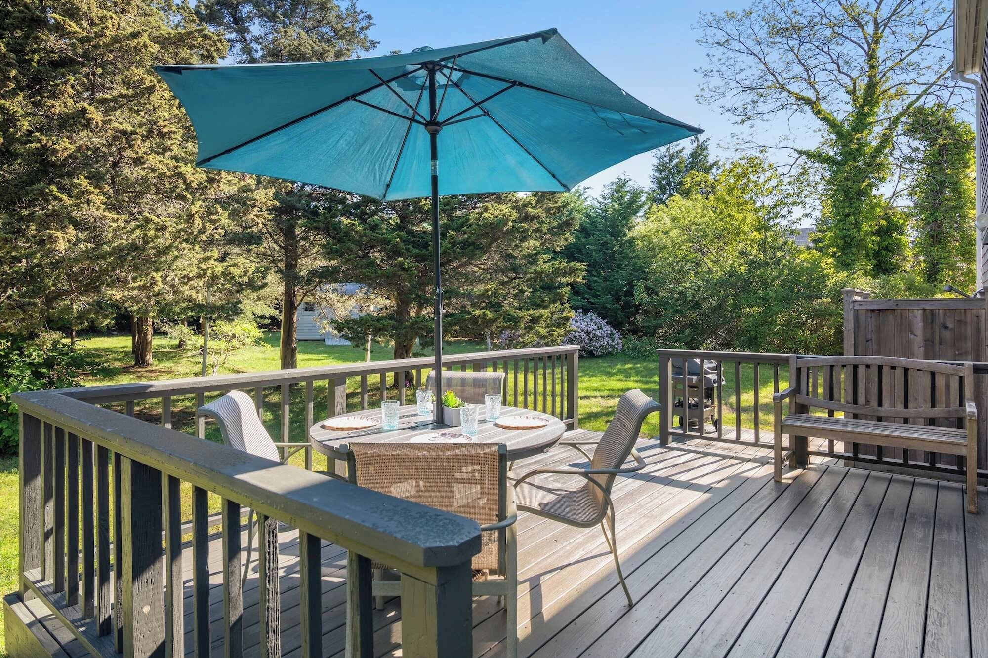 A wooden deck with a table and chairs, a large umbrella, and a grill.