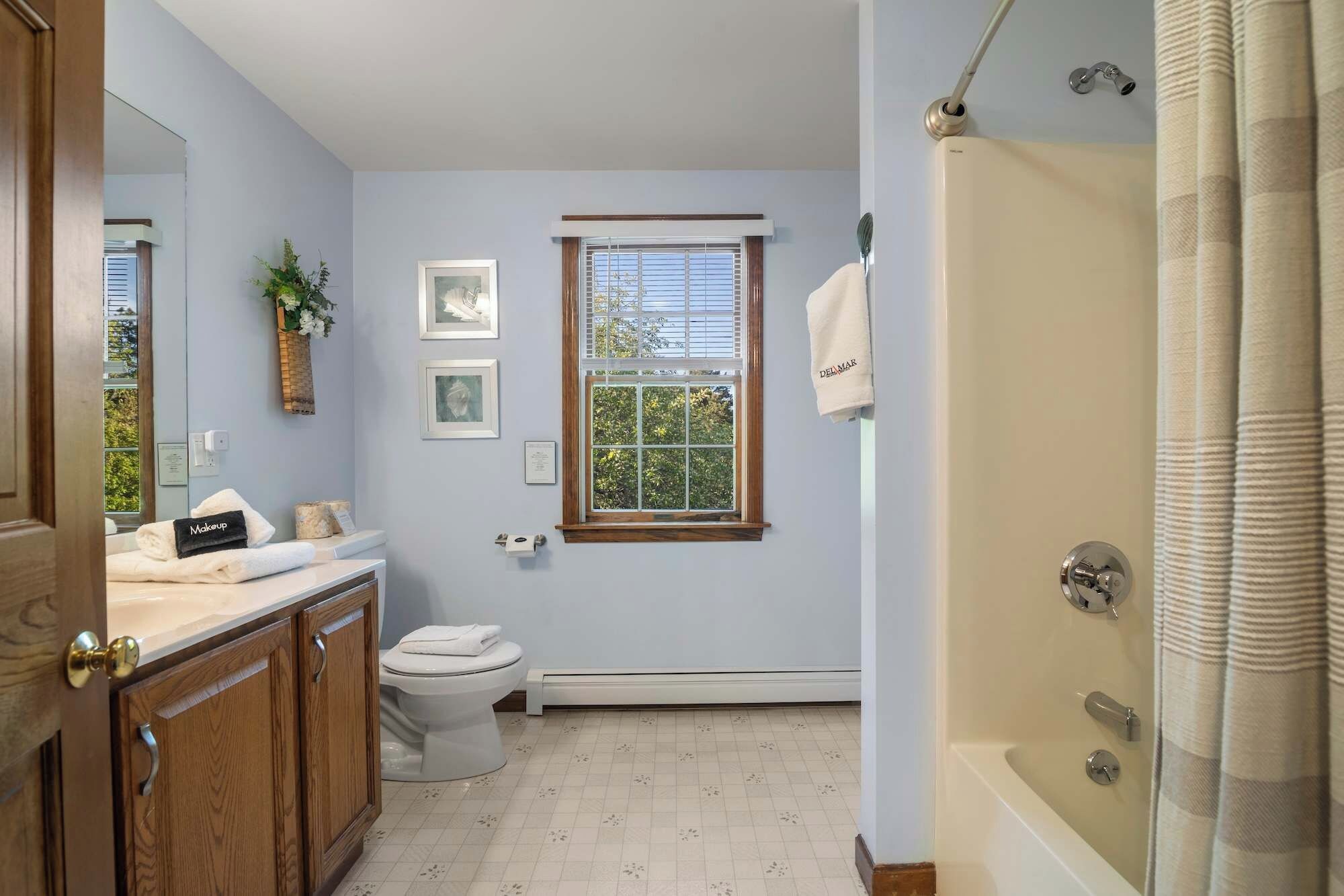 Une salle de bain comprenant des toilettes, un lavabo avec un meuble-vasque, une douche avec un rideau et une fenêtre avec des stores.