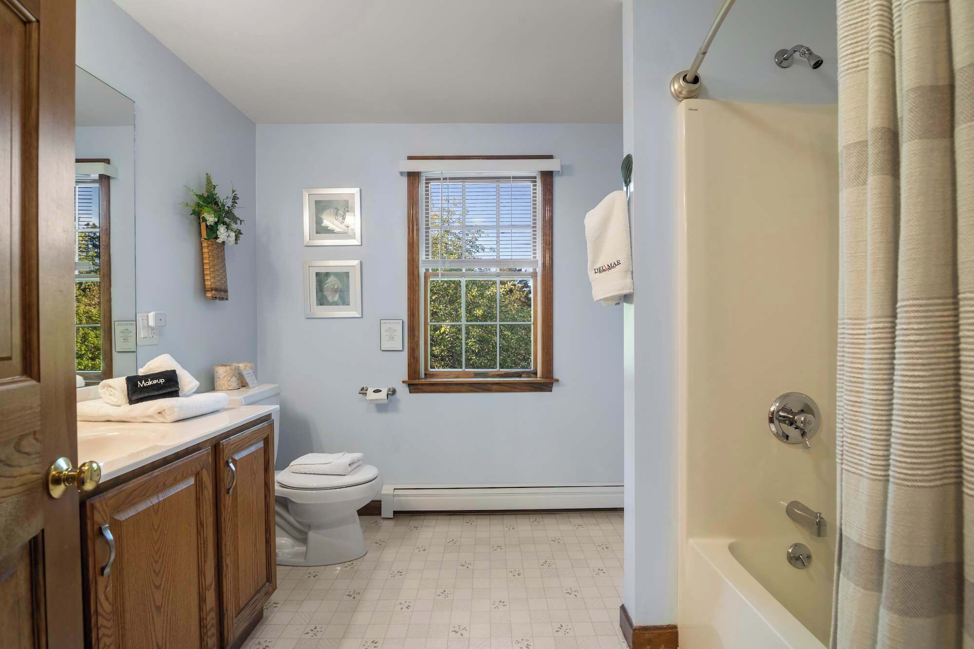 A bathroom with a toilet, a sink with a vanity, a shower with a curtain, and a window with blinds.