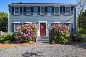 A two-story house with a red door, white trim, and a gravel driveway. - Perfect Relaxation Spot 5 min to Beach! (Eastham)