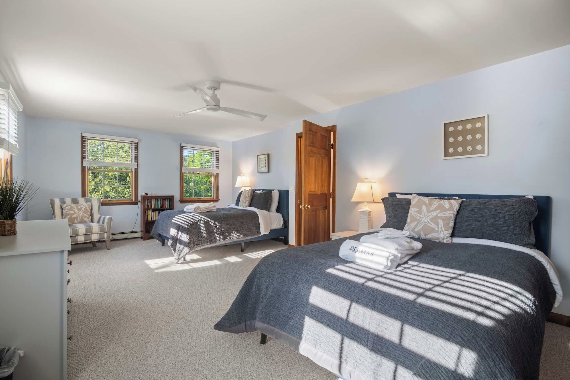 A bedroom with two beds, a ceiling fan, and a large window with blinds.