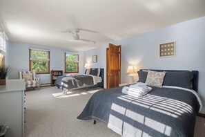 A bedroom with two beds, a ceiling fan, and a large window with blinds.