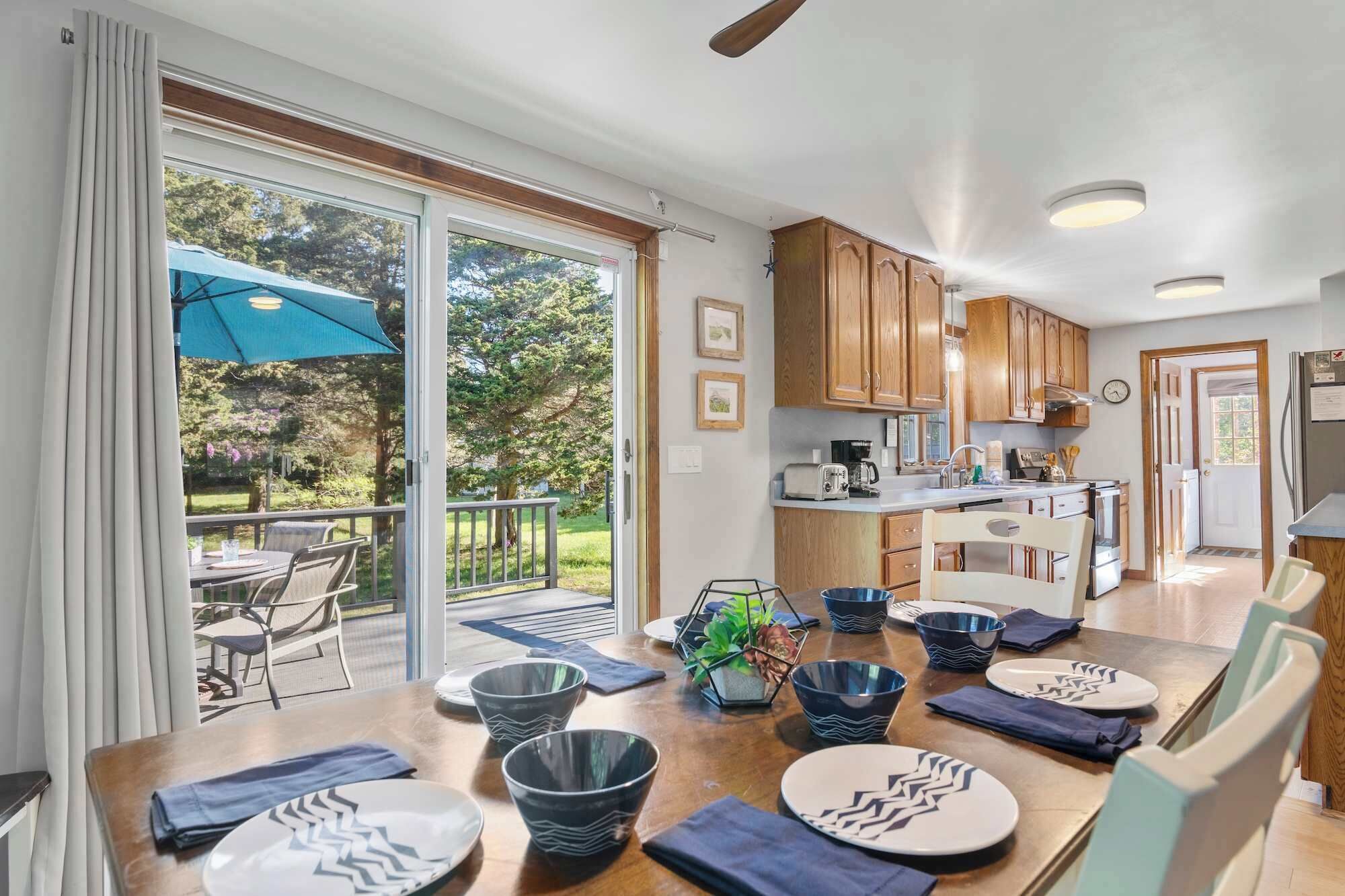 A modern kitchen with wooden cabinets, a dining area with a table set for four, and a patio with a blue umbrella.