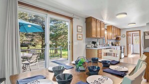 A modern kitchen with wooden cabinets, a dining area with a table set for four, and a patio with a blue umbrella. - Perfect Relaxation Spot 5 min to Beach! (Eastham)