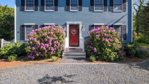 A two-story house with a red door, white trim, and a gravel driveway. - Perfect Relaxation Spot 5 min to Beach! (Eastham)