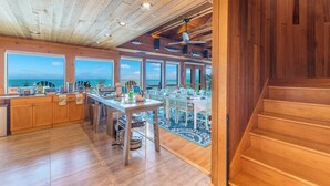 Una cocina amplia con una isla grande, techo de madera y ventanas panorámicas con vistas al océano.
