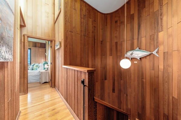 A hallway with wooden paneling, a bed with a nightstand, a wall-mounted fish decoration, and a light fixture.