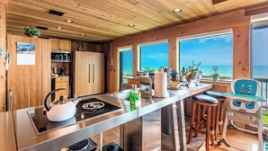 Una cocina moderna con armarios de madera, una isla de acero inoxidable y grandes ventanas con vista al océano.