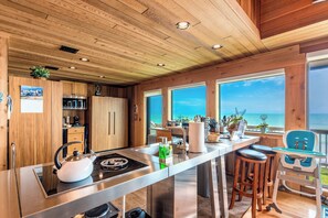 Una cocina moderna con armarios de madera, una isla de acero inoxidable y grandes ventanas con vista al océano.