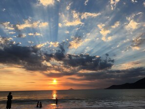 A sunset over a body of water with people in the water and on the shore.