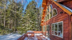 A wooden cabin with large windows, a wooden deck, and a snowy forest backdrop. - Two Winds - Beautiful newer home on Mooselookmeguntic Lake (Rangeley)