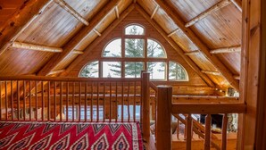 A wooden interior with a high ceiling, a large arched window, and a wooden railing. - Two Winds - Beautiful newer home on Mooselookmeguntic Lake (Rangeley)