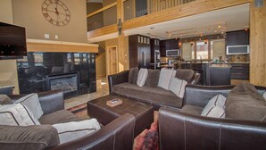 A spacious living area with a fireplace, leather sofas, and a kitchen in the background.