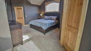 A bedroom with a bed, a wooden wardrobe, a nightstand with a lamp, and a window with a view.